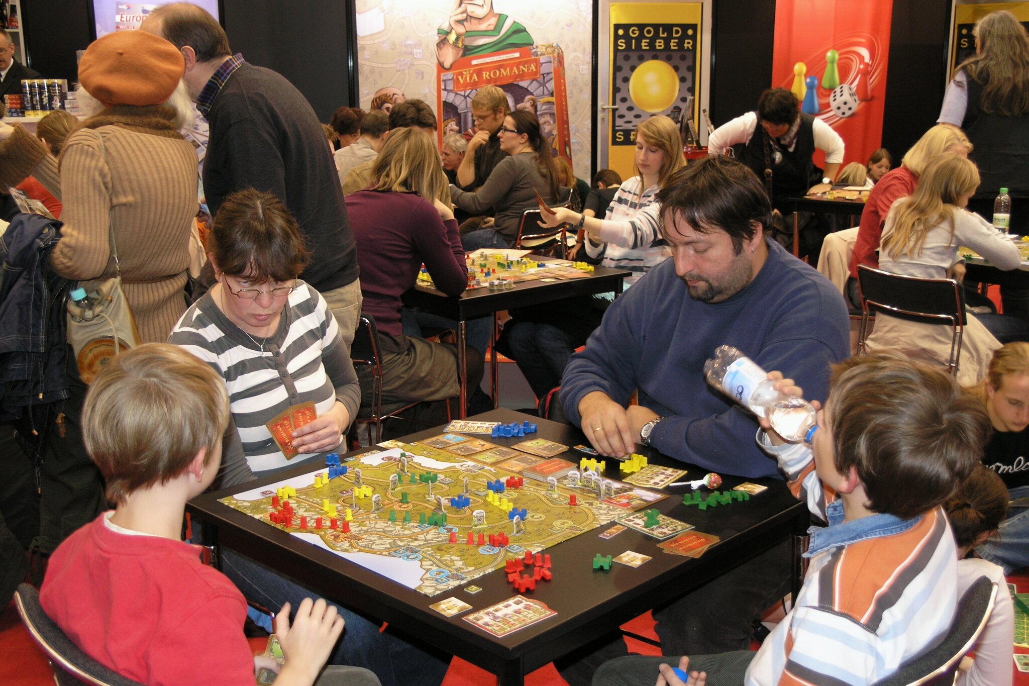 Famiglie con bambini che giocano a più tavoli alla fiera SPIEL di Essen